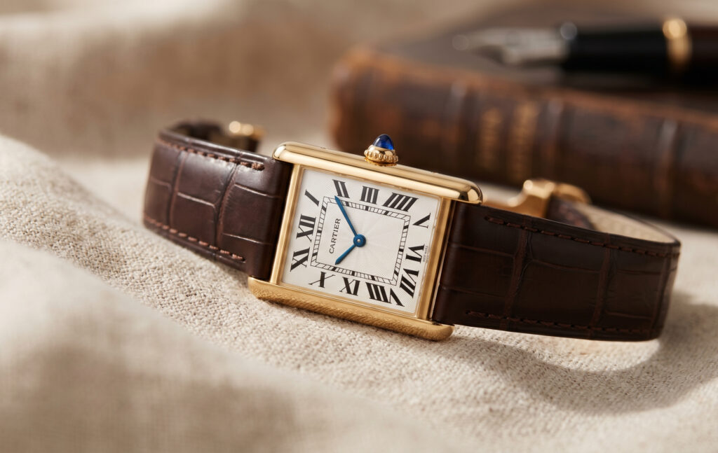 リネン生地の上に置かれた、1917年誕生の普遍的デザイン、カルティエ タンク ルイ カルティエ（ゴールドケース、レザーストラップ）。
