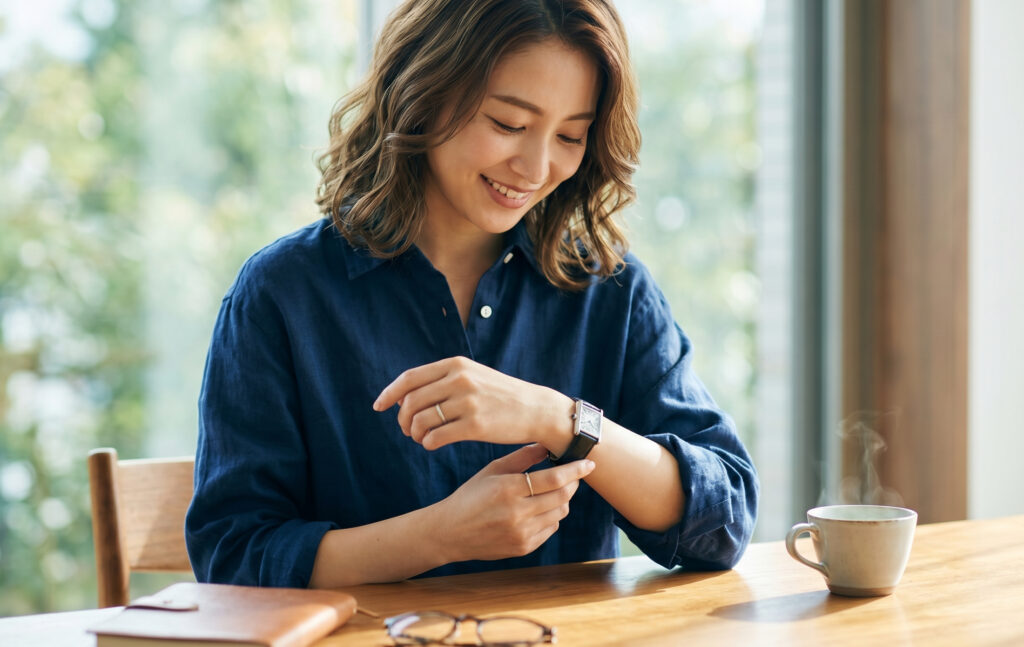 自宅のリラックスした空間で、購入したカルティエのタンクマストウォッチを初めて腕に装着し、嬉しそうに眺める日本人女性。