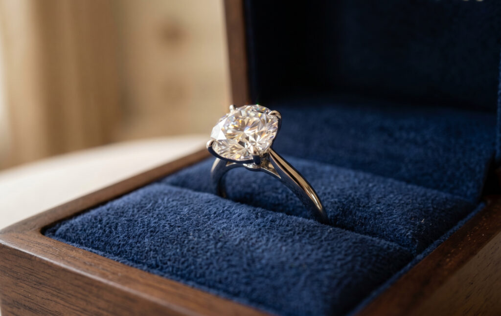 高級感のある木製ボックス内のベルベットクッションに置かれた、まばゆい輝きを放つ高品質なダイヤモンド婚約指輪