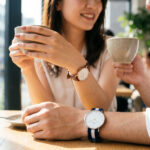 東京のカフェでダニエルウェリントンの時計を着用するアジア人カップル。ローズゴールドのレザーモデルとシルバーのNATOストラップモデルが、カジュアルでおしゃれな雰囲気を演出している