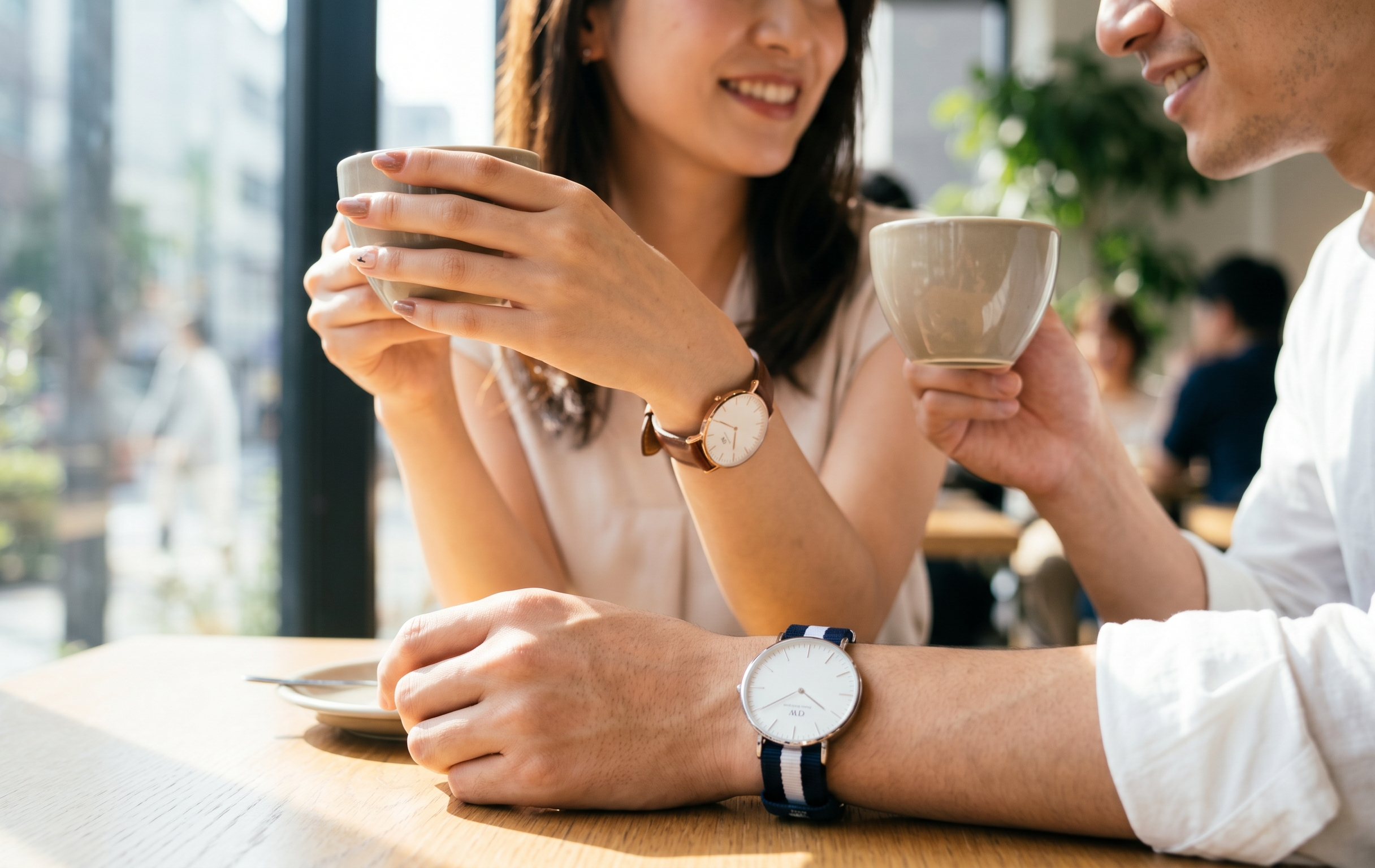 東京のカフェでダニエルウェリントンの時計を着用するアジア人カップル。ローズゴールドのレザーモデルとシルバーのNATOストラップモデルが、カジュアルでおしゃれな雰囲気を演出している