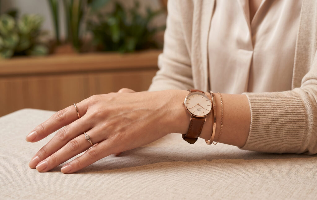 東京のカフェで、ダニエルウェリントンの時計とローズゴールドのバングル、上品な指輪を巧みに重ね付けした、エレガントなアジア人女性の手元。計算された大人のラグジュアリー感が漂う。