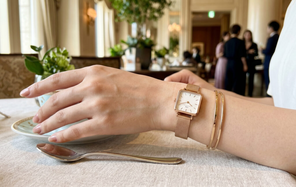 東京の高級ホテルで開催されたアフタヌーンティーにて、ダニエルウェリントンのスクエア型「Quadro」のローズゴールドメッシュモデルを着用する、エレガントなアジア人女性の手元。繊細で女性らしい魅力を際立たせている。