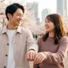 桜並木を笑顔で歩く日本人カップル。繋いだ手にはシンプルなペアリングが光り、2人の絆と幸せを象徴している