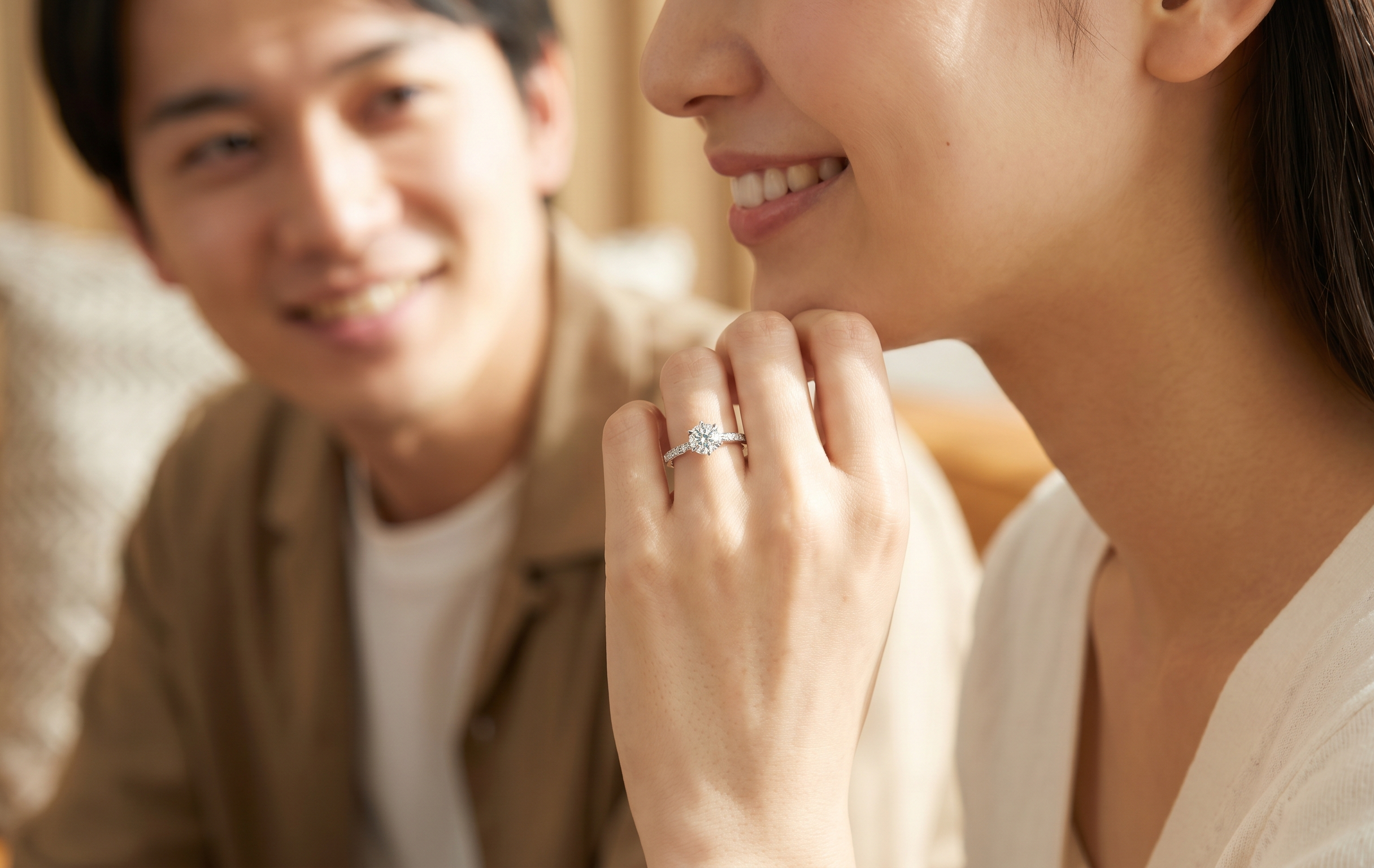 日本人の若いカップルが笑顔で婚約指輪を見つめる、幸せあふれる瞬間を捉えた写真。プラチナとダイヤモンドのリングが光る。