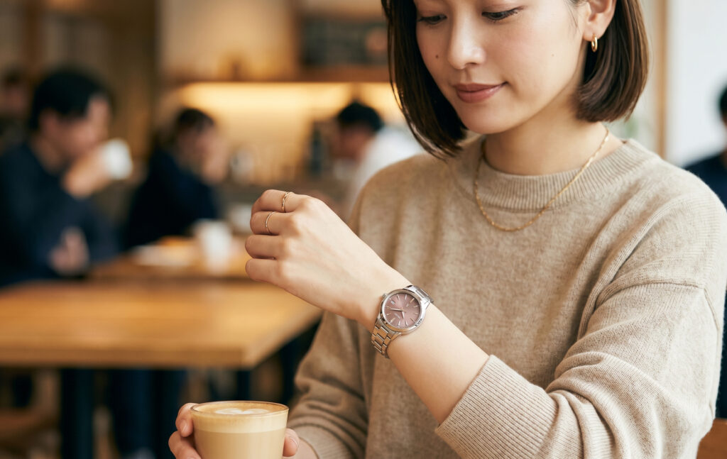 40代の日本人女性が、ネイビーのジャケットを着用し、上品なセイコールキアの時計を身に着けている。落ち着いた雰囲気のオフィスラウンジで自信を持って微笑んでおり、大人の女性に似合う時計であることを示している。