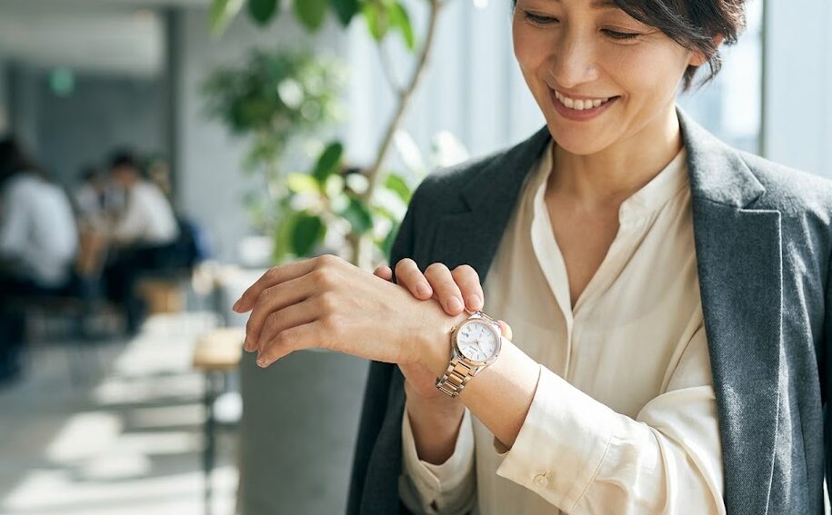柔らかな光が差し込む現代的なカフェで、40代後半の日本人女性が、自信に満ちた笑顔で自身の腕元のセイコールキアの時計（ラボグロウンダイヤモンド入り）を見つめている。彼女のグレーのジャケットと洗練された雰囲気が、時計は大人の女性を輝かせるアイテムであることを証明している。