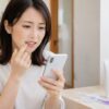 アクニーホワイトニングの口コミや効果をスマホで調べながら歯を気にする日本人女性
