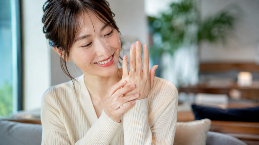 自然光の中、婚約指輪を光にかざし、ダイヤのきらめきをうっとりと見つめる日本人女性の手元。多角的な検証の開始とブランドの多様な魅力を提示