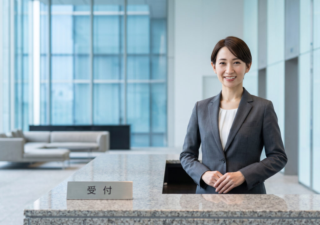 東京都港区の近代的な高層ビル内にある、メビウス製薬のオフィス受付で微笑む日本人女性従業員