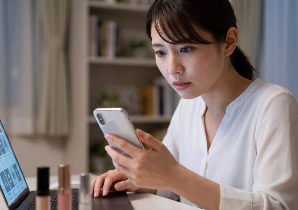 深夜、スマホとPCを使い、複数のオンラインショップでスノービューティーの在庫を必死に探す、真剣な表情の日本人女性