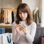 おしゃれな服を前にスマホを見て悩む日本人女性