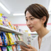 コンビニの飴売り場で、スマートフォンを片手に目的の商品を探している日本人女性