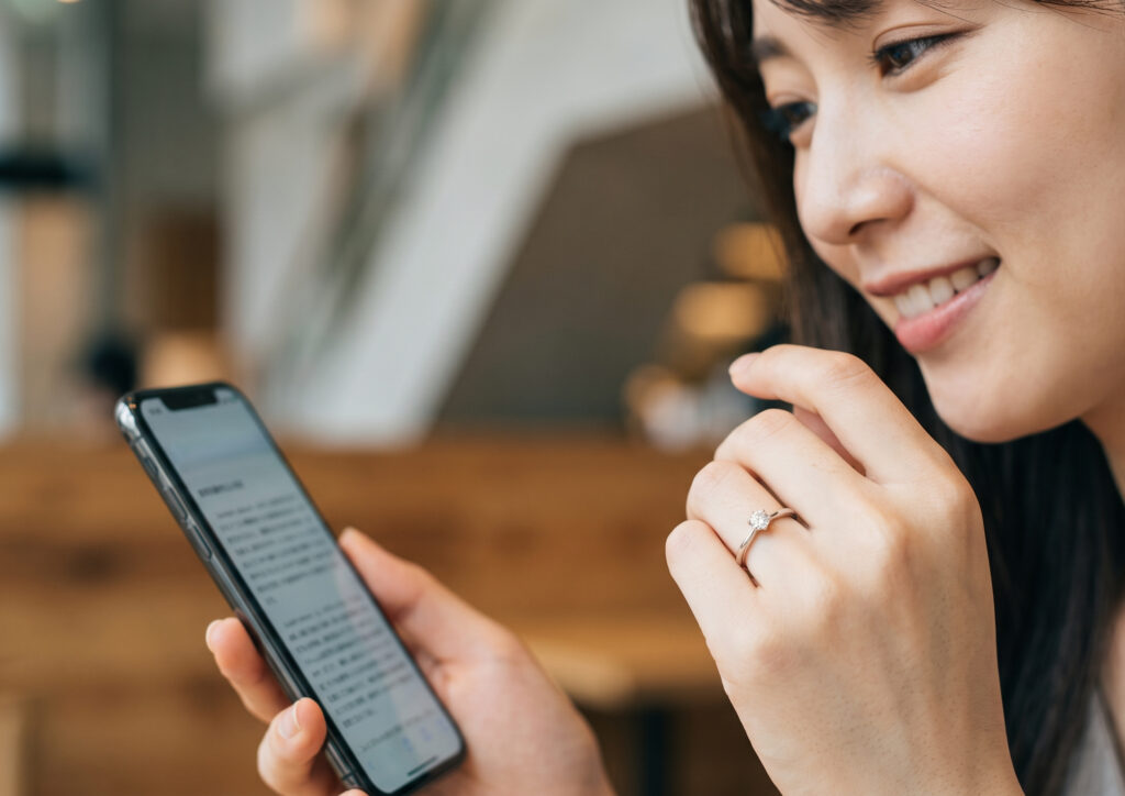 スマホでネガティブワードの自動表示に関する解説を読み、安堵した表情で自分の洗練された婚約指輪を見つめる日本人女性