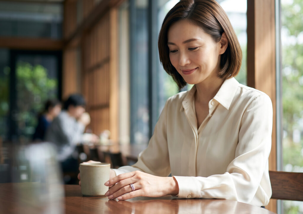 落ち着いた雰囲気のカフェで、自分の手元の洗練された婚約指輪と結婚指輪を愛おしそうに見つめる落ち着いた日本人女性